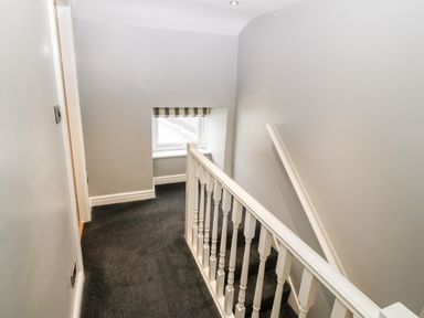 A stairwell with white railing gray walls and a window with a striped blind at Haddef in Nefyn