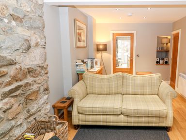 A living room with a checkered sofa stone wall and wooden floor at Haddef in Nefyn