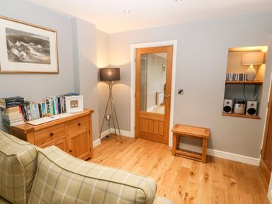 A corner of a room with a wooden sideboard filled with books a wooden stool a floor lamp a wooden door and a small shelf with a stereo and a lamp at Haddef in Nefyn