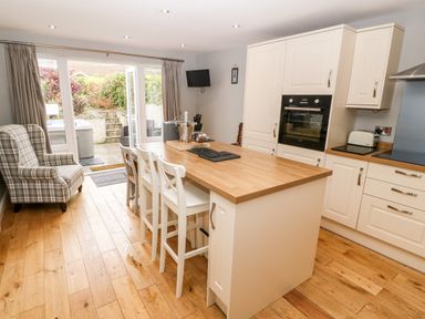 A kitchen with a wooden island and white chairs next to a door leading outside to a garden at Haddef in Nefyn