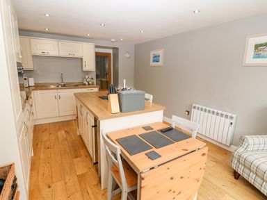 A kitchen with wooden floors and white cabinets a wooden table with gray placemats and chairs at Haddef in Nefyn