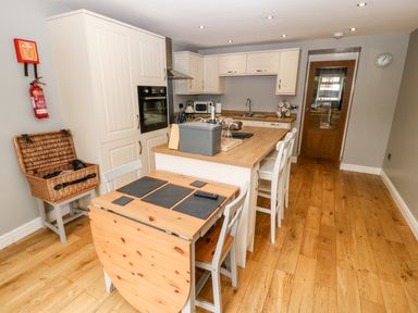A kitchen with wooden floor white cabinets and a wooden table with chairs at Haddef in Nefyn