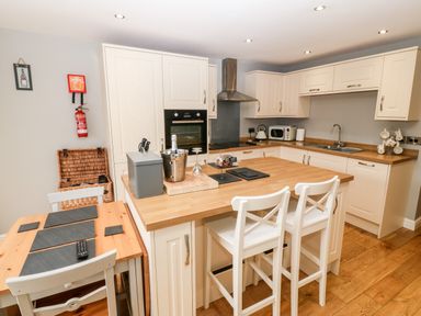 A kitchen with wooden countertops white cabinets and stools at Haddef in Nefyn