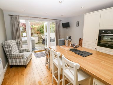A kitchen with a wood countertop island and white chairs next to glass doors opening to a patio at Haddef in Nefyn