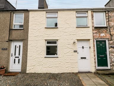 The front of a cream stone textured terraced house with white door and three windows at Haddef in Nefyn