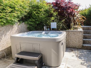 An outdoor hot tub with steps surrounded by greenery and plants at Haddef in Nefyn