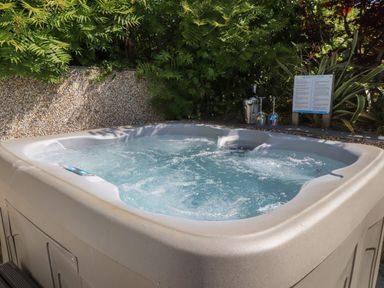 An outdoor hot tub with bubbling water surrounded by plants and a stone wall at Haddef in Nefyn