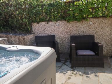 An outdoor seating area with two woven chairs and a hot tub on a stone patio at Haddef in Nefyn