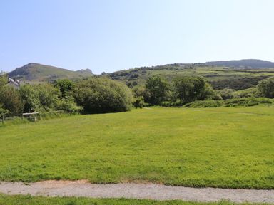 A grassy open field with trees and hills in the background at Haddef in Nefyn