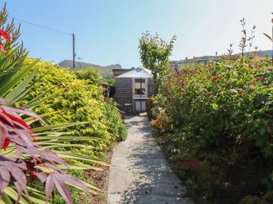 A garden path leading to a wooden shed with an umbrella in Haddef Nefyn