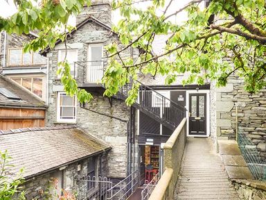 Stone buildings with external stairs and a walkway surrounded by green tree branches at High Ridge in Ambleside