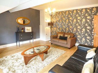 A living room with a brown sofa black sofa wooden coffee table and a patterned wall at High Ridge in Ambleside