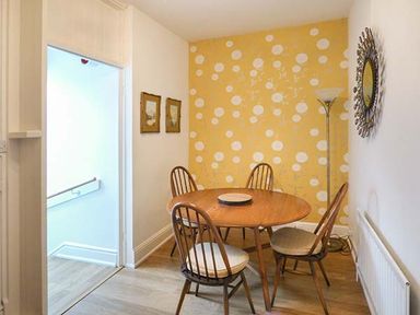 A dining area with a round wooden table and four wooden chairs against a yellow patterned accent wall at High Ridge in Ambleside