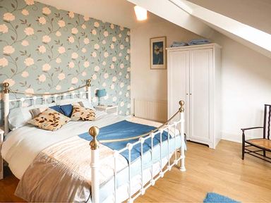 A bedroom with a metal bed frame blue floral wallpaper white wardrobe and wooden chair at High Ridge in Ambleside