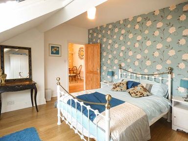 A bedroom with a white metal bed frame blue and white bedding floral wallpaper and a wooden door at High Ridge in Ambleside