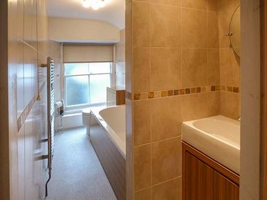 A bathroom with a bathtub a toilet a sink and a frosted window at High Ridge in Ambleside