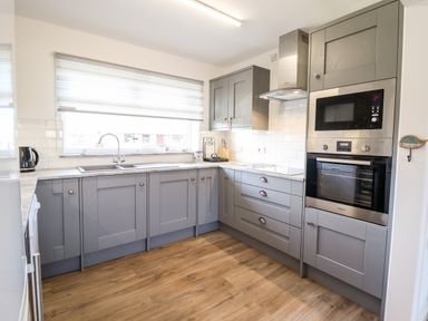 A kitchen with gray cabinets wooden floor and built in oven and microwave at Sealyons Fairbourne near Dolgellau