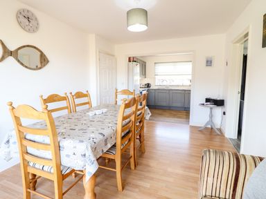 A dining area with wooden chairs and a table with a patterned tablecloth next to a kitchen with gray cabinets at Sealyons Fairbourne near Dolgellau