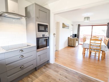 A kitchen with gray cabinets and built-in oven next to a dining area with wooden table and chairs at Sealyons Fairbourne near Dolgellau