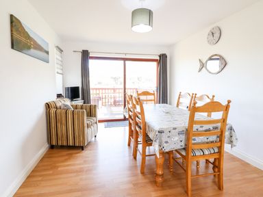 A dining room with a wooden table and chairs a striped armchair and a sliding glass door at Sealyons Fairbourne near Dolgellau