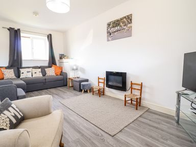 A living room with sofas chairs a television and a wall-mounted fireplace at Sealyons in Fairbourne near Dolgellau