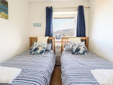 A bedroom with two single beds and blue striped bedding with a window in between at Sealyons Fairbourne near Dolgellau