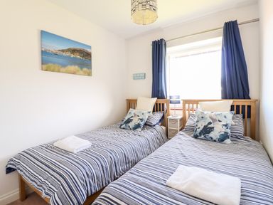 A bedroom with two single beds striped bedding and a window with blue curtains at Sealyons in Fairbourne near Dolgellau