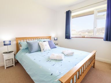A bedroom with a wooden bed blue bedspread pillows bedside tables and a window with blue curtains at Sealyons Fairbourne near Dolgellau