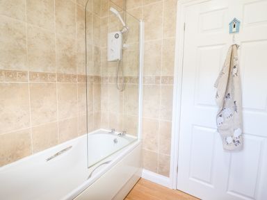 A bathroom with a bathtub and shower next to a white door with a towel hanging at Sealyons Fairbourne near Dolgellau