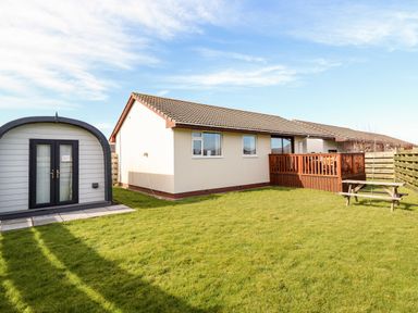 A backyard with a single story house a wooden deck a small shed with double doors and a picnic bench at Sealyons in Fairbourne near Dolgellau
