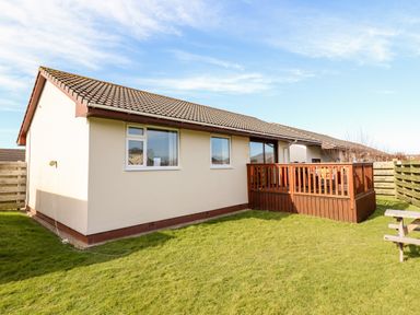 The exterior of a single-story house with a tiled roof wooden deck and fenced grassy yard at Sealyons Fairbourne near Dolgellau