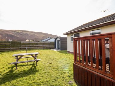 A wooden picnic table on a grass lawn next to a house with a wooden deck at Sealyons in Fairbourne near Dolgellau