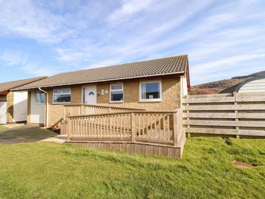 A single story house with a wooden ramp and a lawn at Sealyons Fairbourne near Dolgellau