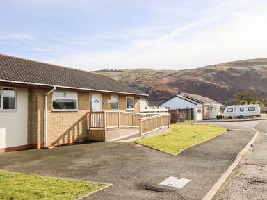 A single story house with a ramp and a driveway near a road with hills in the background at Sealyons in Fairbourne near Dolgellau
