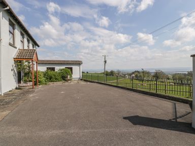 A paved driveway next to a white house with plants and a metal fence overlooking a green field at Moors Farm in Littledean