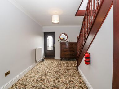 A hallway with floral carpet a wooden staircase a chest of drawers and a round mirror at Moors Farm in Littledean