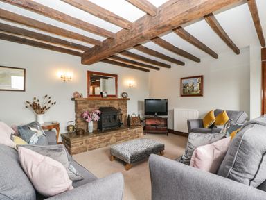 A living room with wooden beams stone fireplace grey sofas and a television at Moors Farm in Littledean