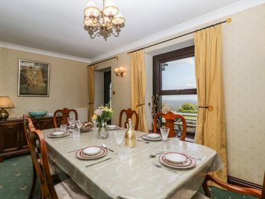 A dining room with a set table and wooden chairs near windows with yellow curtains at Moors Farm in Littledean