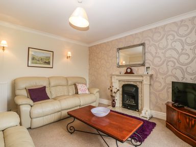 A living room with beige leather sofas a wooden coffee table a fireplace with a mirror above and a television on a wooden stand at Moors Farm in Littledean