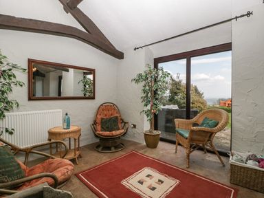 A sunroom with wicker chairs a red rug a small table and large sliding glass doors at Moors Farm in Littledean