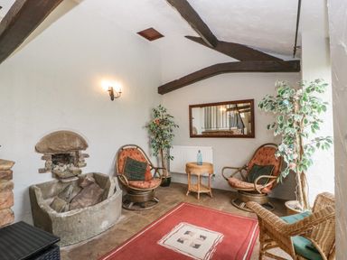 A small sitting area with two cushioned chairs a wicker chair a small table a stone fireplace and plants at Moors Farm in Littledean