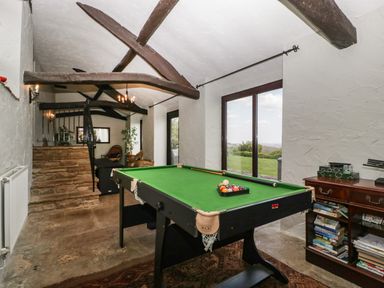 A game room with a pool table and bookshelf next to large windows at Moors Farm in Littledean