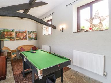 A game room with a pool table two wicker chairs a wooden cabinet and paintings on the walls at Moors Farm in Littledean
