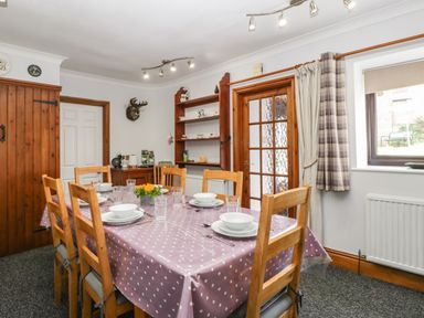 A dining room with a wooden table set for six and wooden chairs near a window and wooden door at Moors Farm Littledean