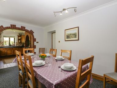 A dining room with a table set for six and a polka dot tablecloth next to a kitchen with wooden cabinets at Moors Farm in Littledean