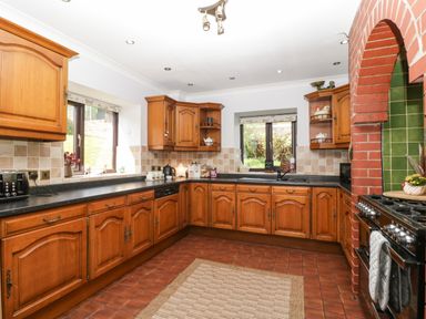 A kitchen with wooden cabinets black countertop tiled backsplash and floor at Moors Farm in Littledean