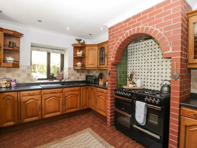 A kitchen with wooden cabinets a black stove under a brick arch and a window above a black sink at Moors Farm in Littledean