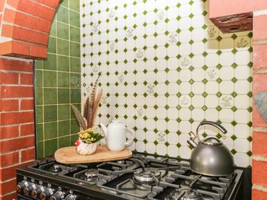 A stove with a kettle a white teapot and a small vase with flowers and feathers on a cutting board at Moors Farm in Littledean