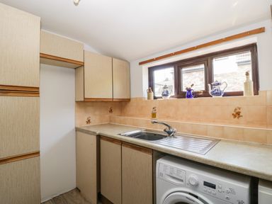A kitchen with wooden cabinets a stainless steel sink washing machine and a window with decorative items on the sill at Moors Farm in Littledean