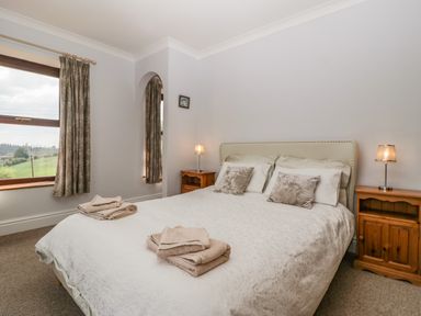 A bedroom with a double bed two bedside tables with lamps and a window with curtains at Moors Farm in Littledean